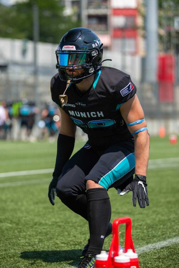Football player in black uniform, face obscured by tinted visor, ready to play.