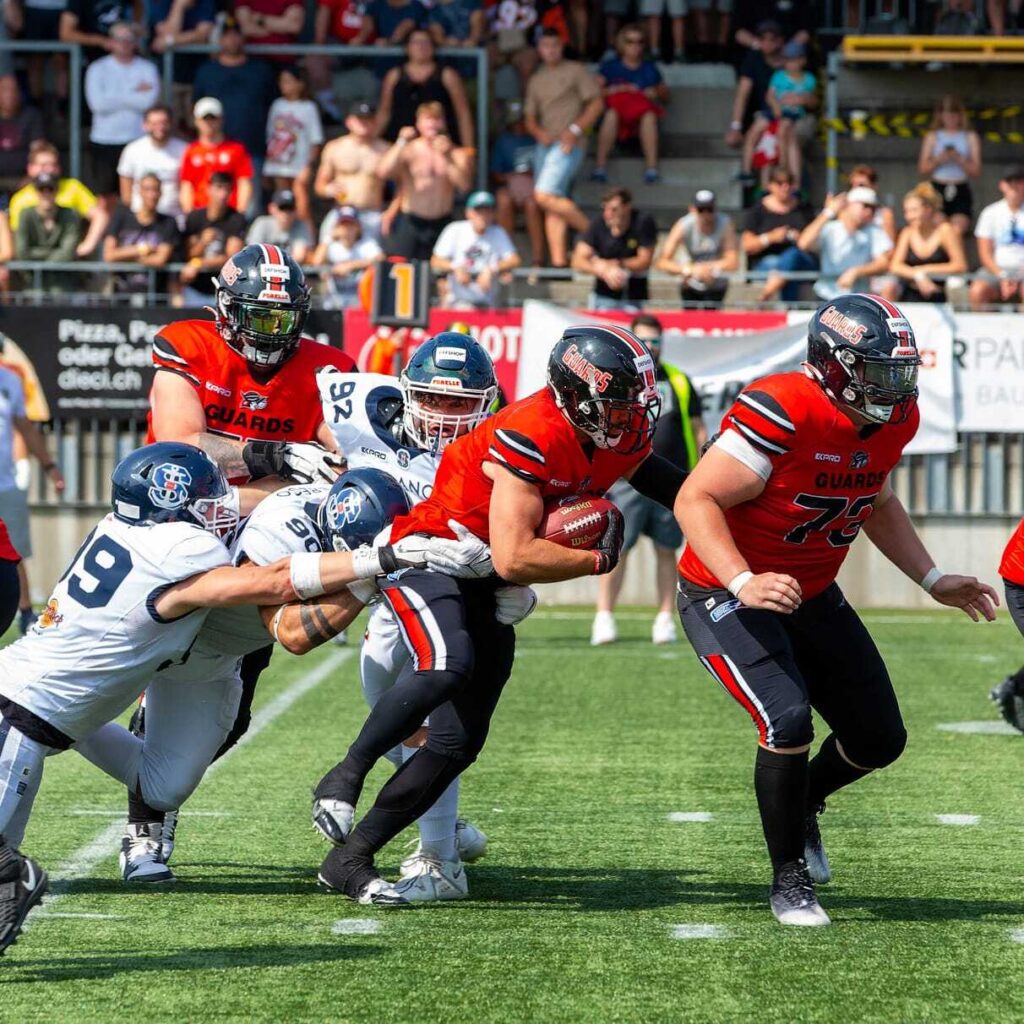 Football players in action, Guards team in orange, Forelle defense closing.