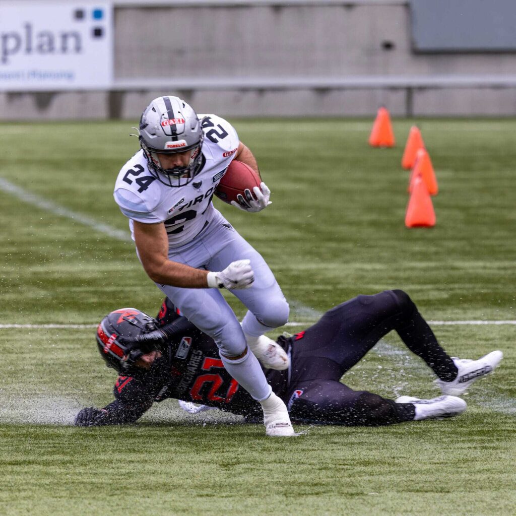 Football player evades a tackle, running with the ball downfield.