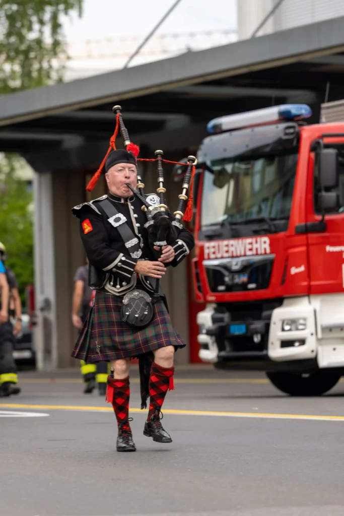 Bagpipe player in traditional Scottish attire performing at a firefighter event