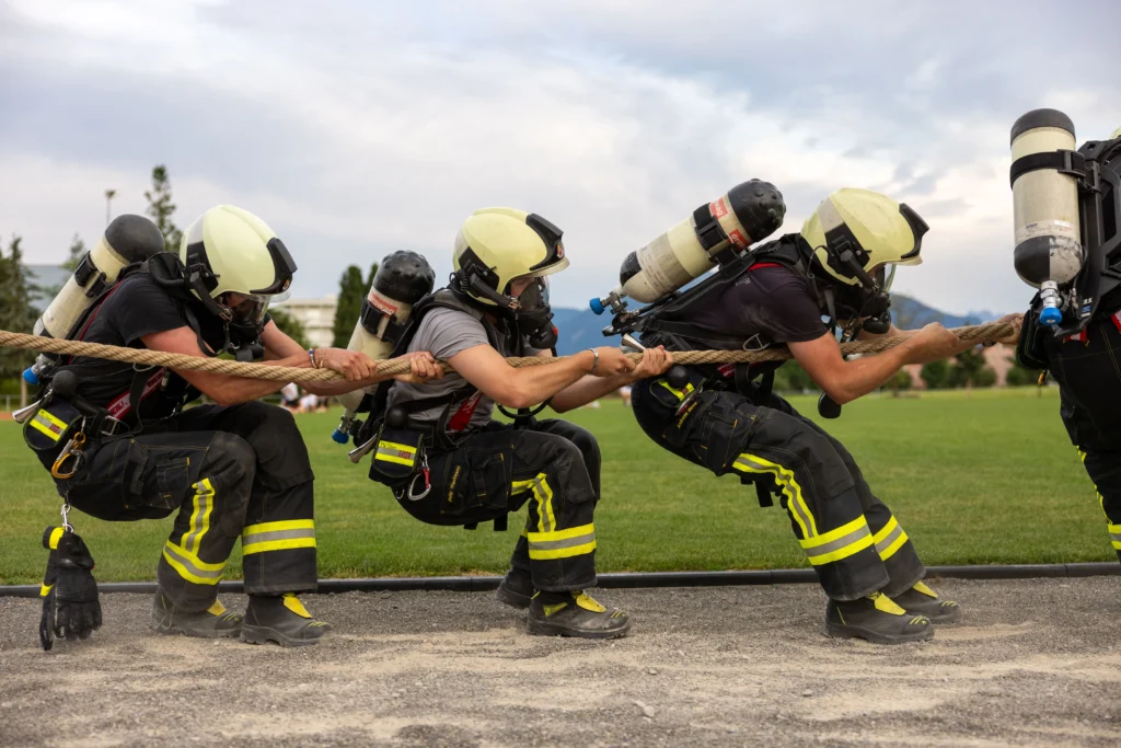 Firefighters in full gear competing in a rope pulling competition on a green field