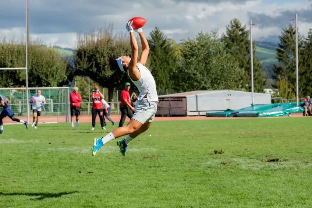 Football player makes impressive catch, leaping high with arms extended in the air.