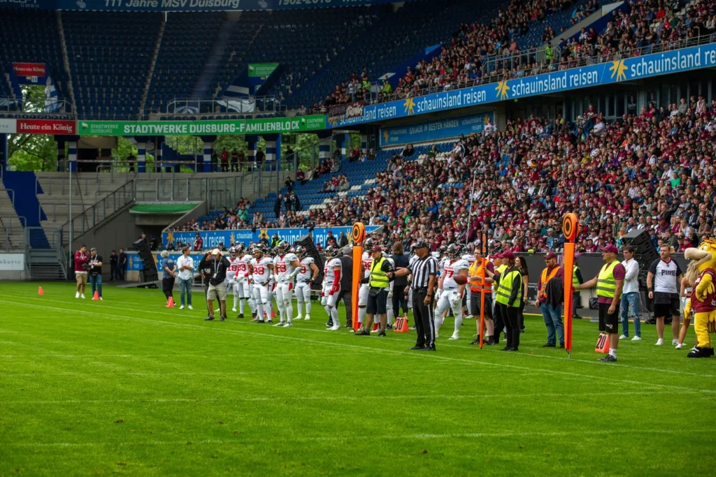 American football players and officials lined up on a green football field.