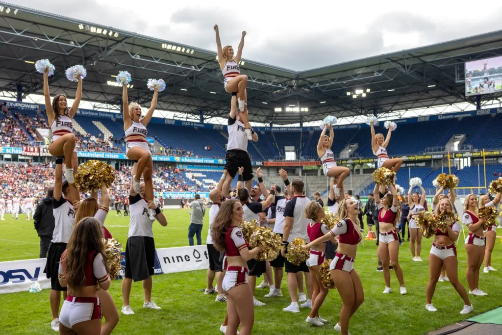Cheerleading squad performs stunts during a football game in a packed stadium.