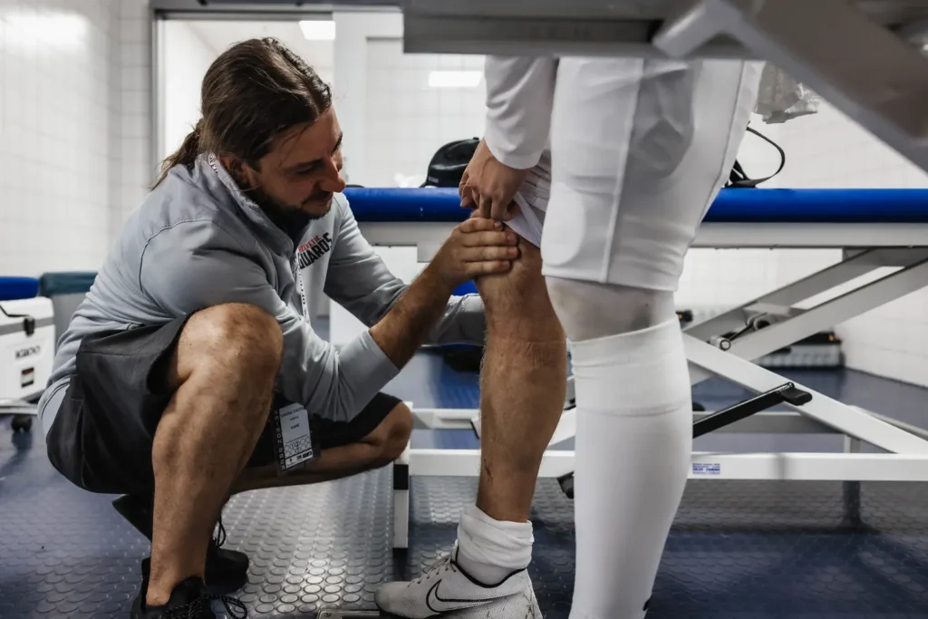 Athlete's knee being examined by trainer, possibly assessing a sports injury.