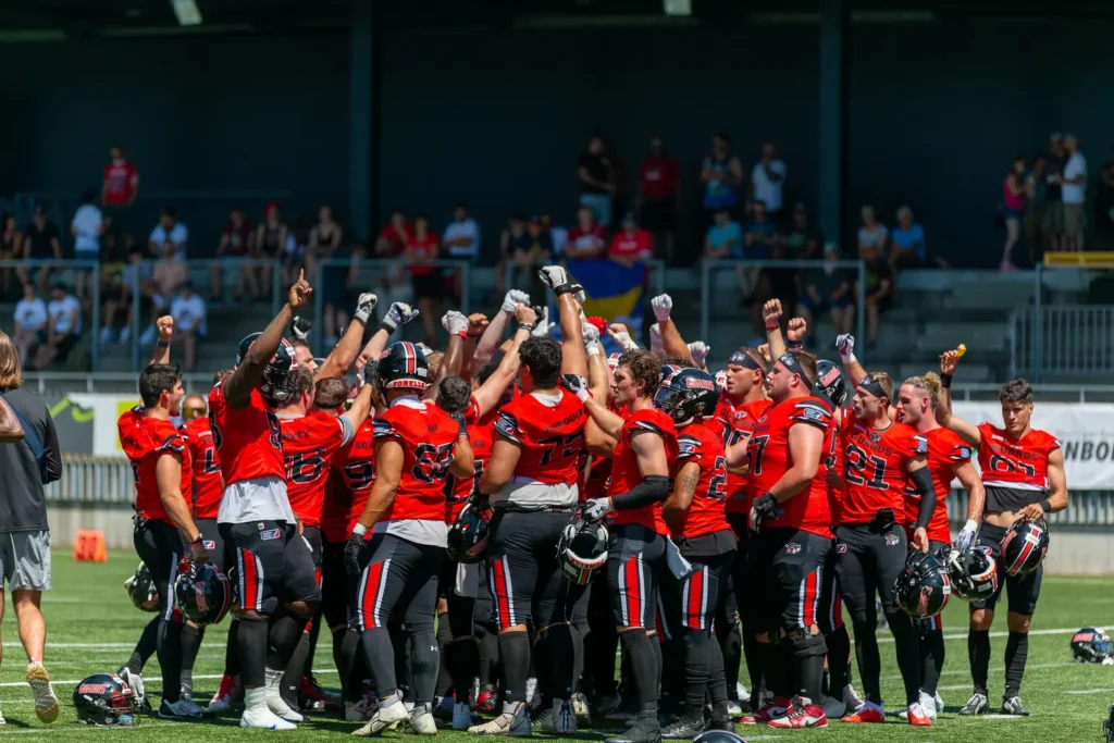 American football team celebrating a win on the field, arms raised.