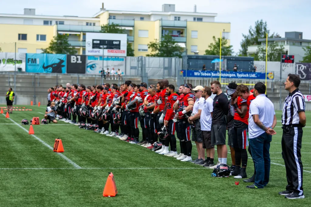 American football team in red stands attentively on a green sports field.