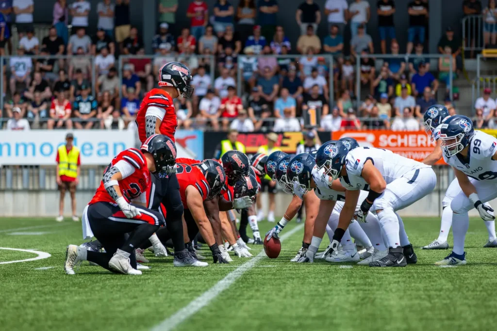 American football teams, Guards and Milano, face off at the scrimmage line.