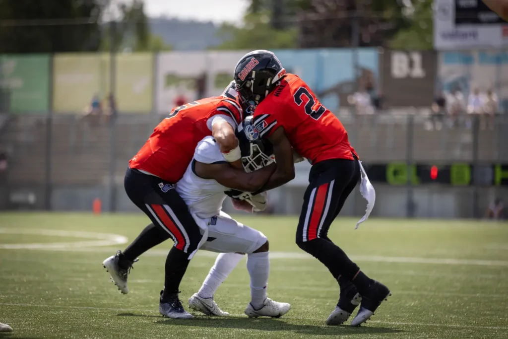 American football players tackling the runner, bright sunlight, green field.