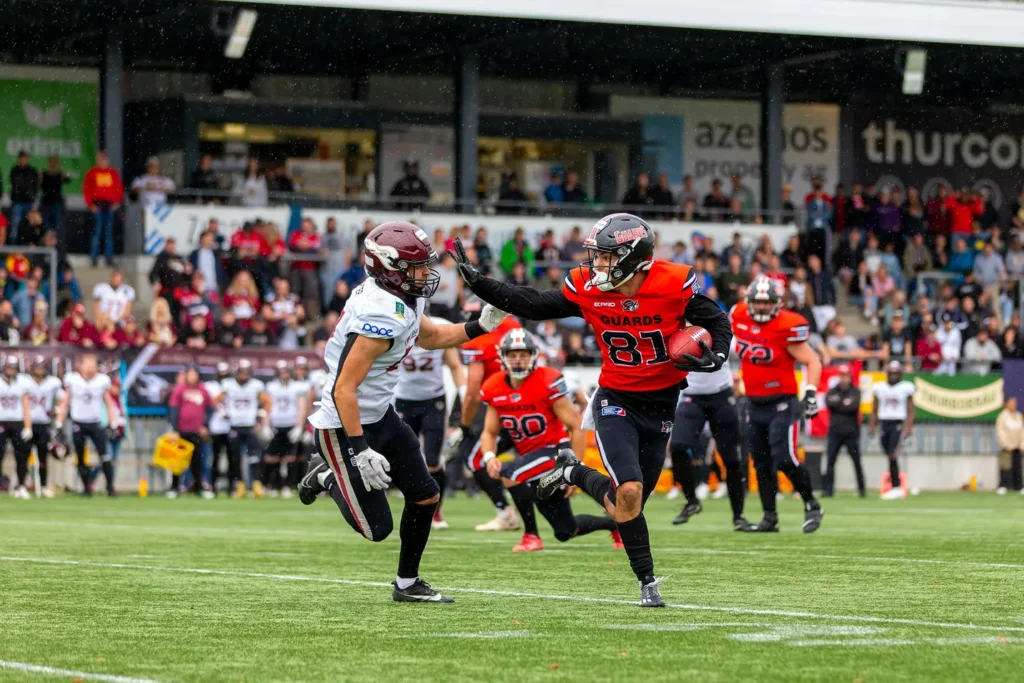 American football player with ball running during rainy game, opponents nearby.