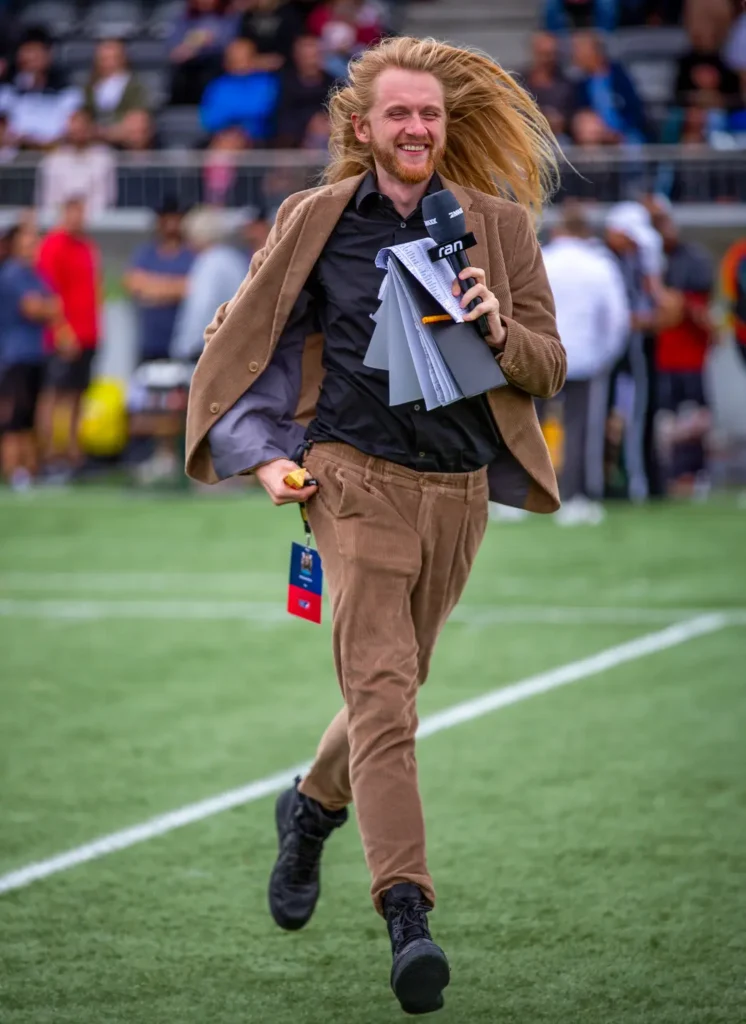 Sidelines reporter running with microphone and notes on the football field.