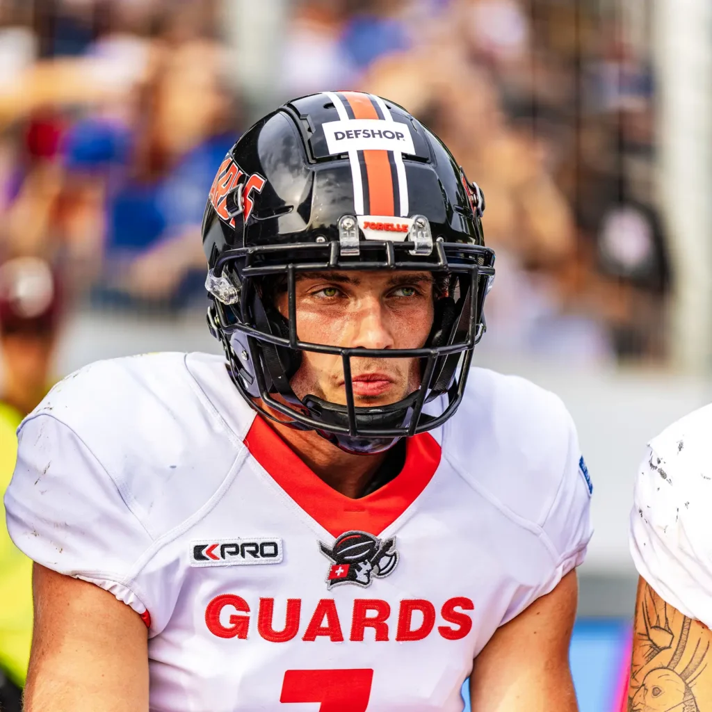 Football player in uniform, intense gaze, wearing helmet and shoulder pads.