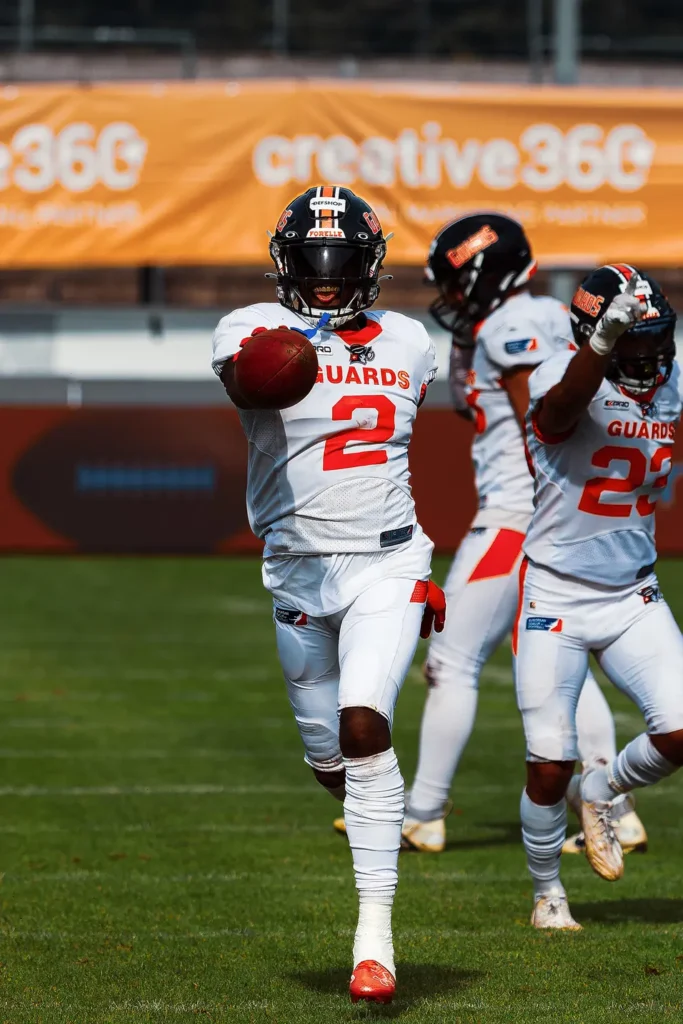 Football player in white uniform throws a football, intense game preparation.