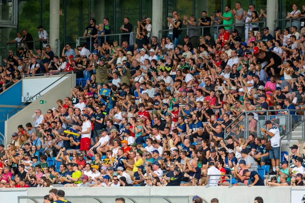 Large crowd applauds enthusiastically in stadium stands, celebrating a sporting event.
