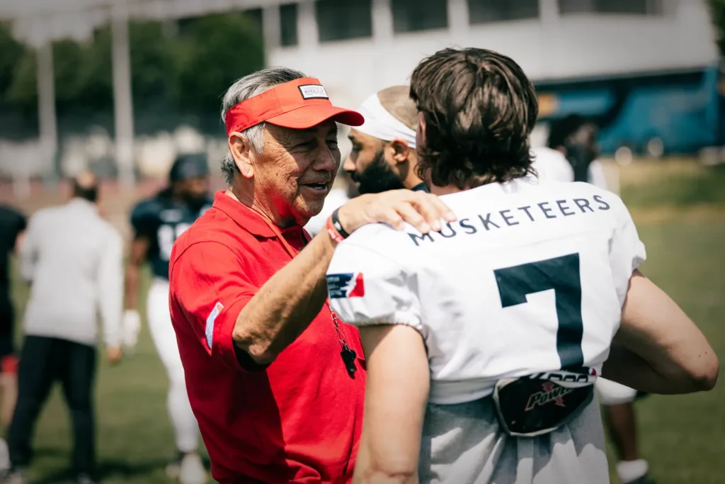 Football coach in red encouraging player wearing number seven uniform, outdoors.