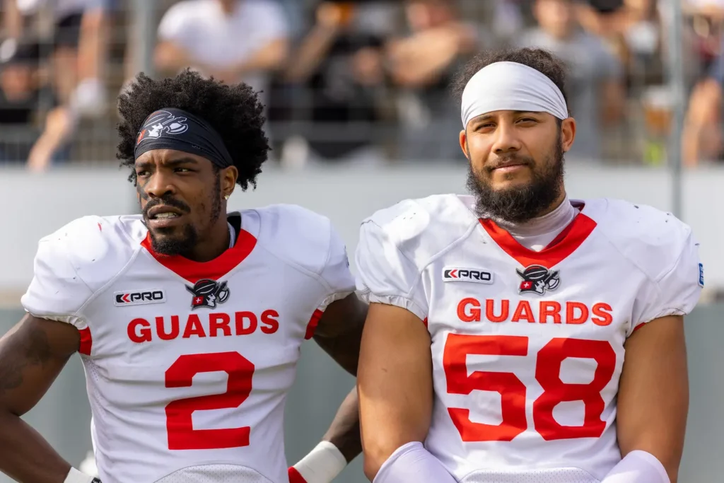 Two football players in white Guards uniforms stand side-by-side outdoors.