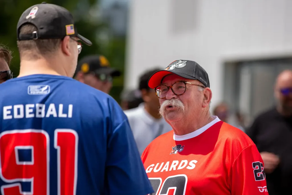 Two men in baseball jerseys converse outdoors, supporting their team.