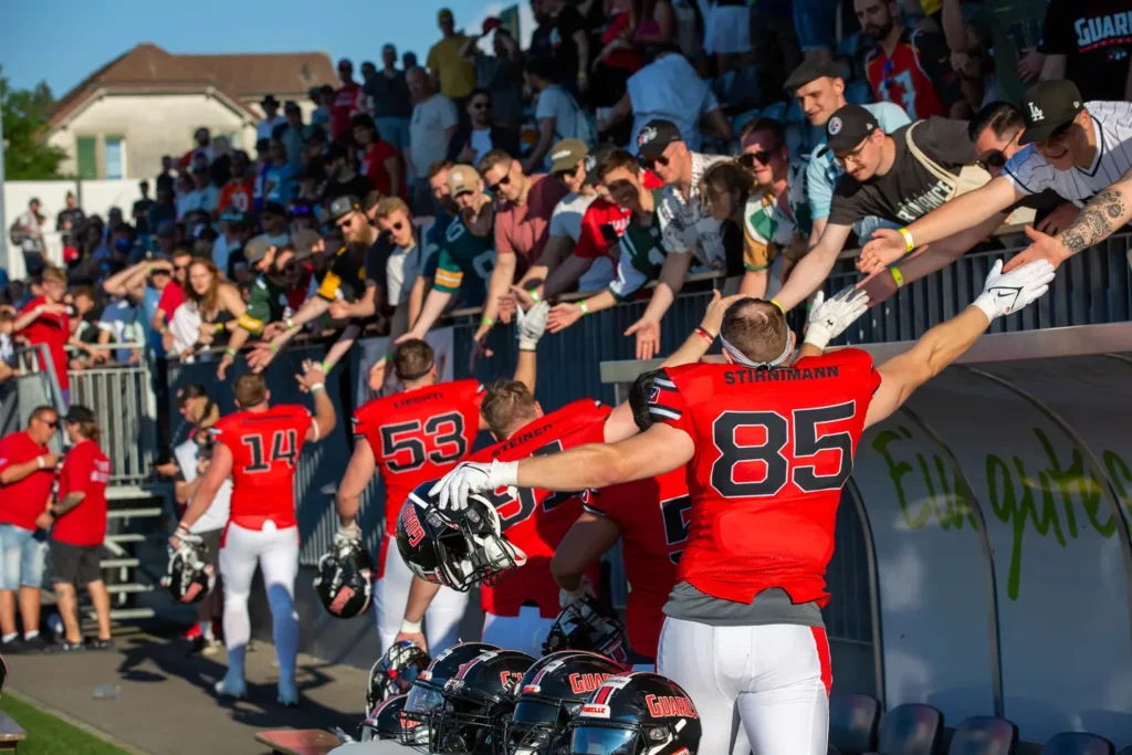 American football players in red uniforms high-fiving fans at a game.