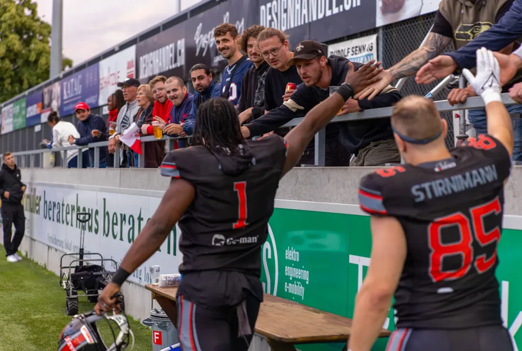 Football players high-fiving fans after a game; player with dreadlocks.
