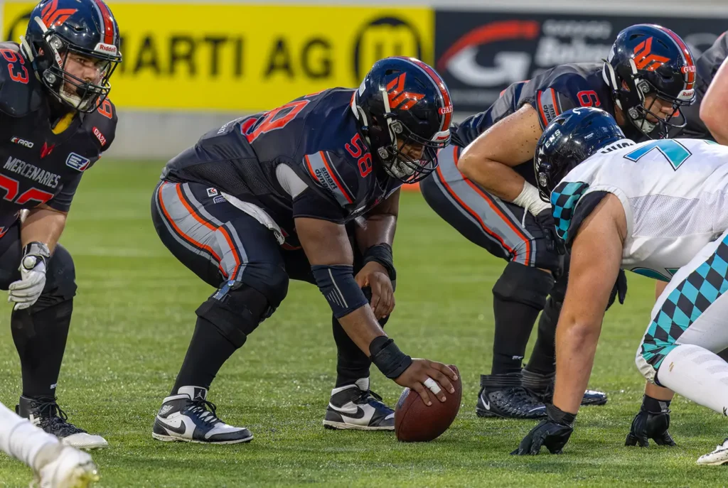 American football players in a ready stance on the line of scrimmage.