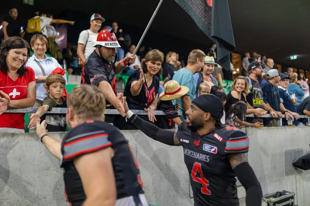 Football player in black uniform high-fiving fans along stadium barrier after game.