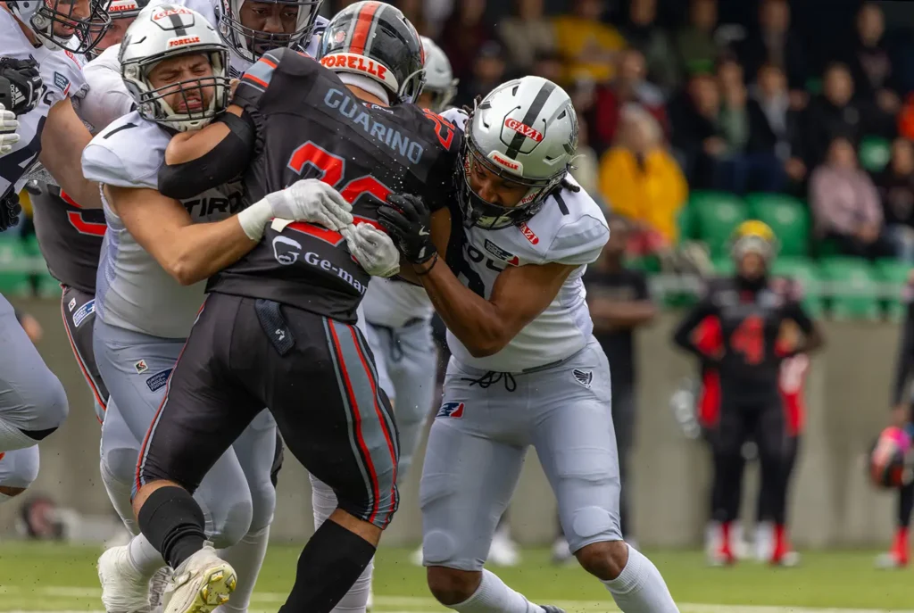 Football player in gray tackling player in black uniform during game action.