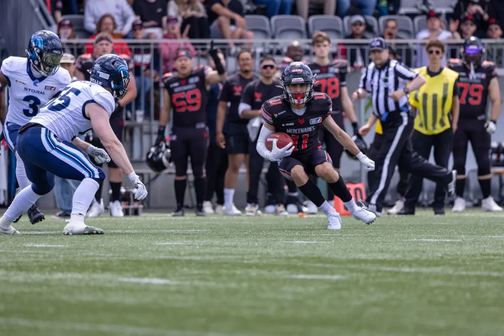 Football player in black uniform running with the football on the field.