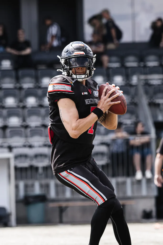 Football player in black uniform, helmet holding ball preparing to throw.