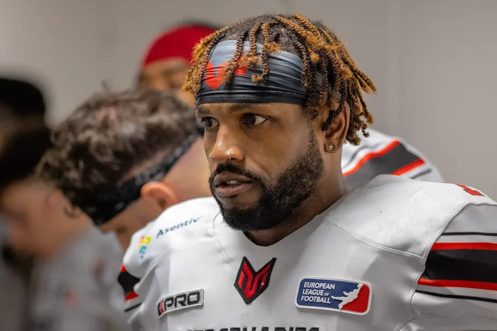 Football player with dreadlocks, headscarf, and piercing in team uniform, focused.