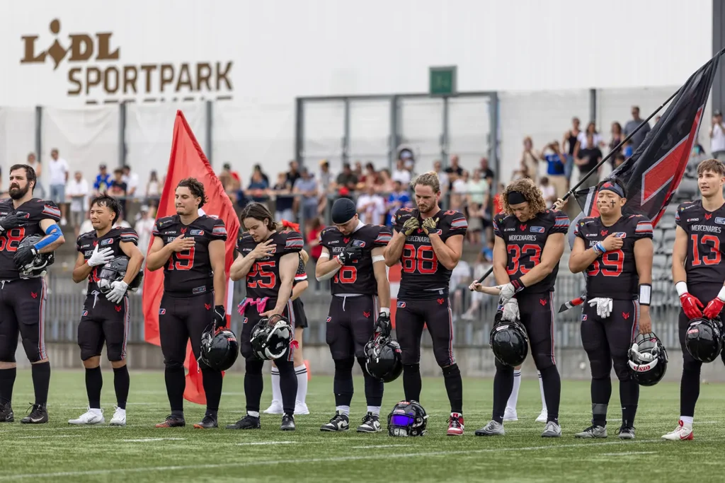 American football players stand solemnly with hands over their hearts on the field.