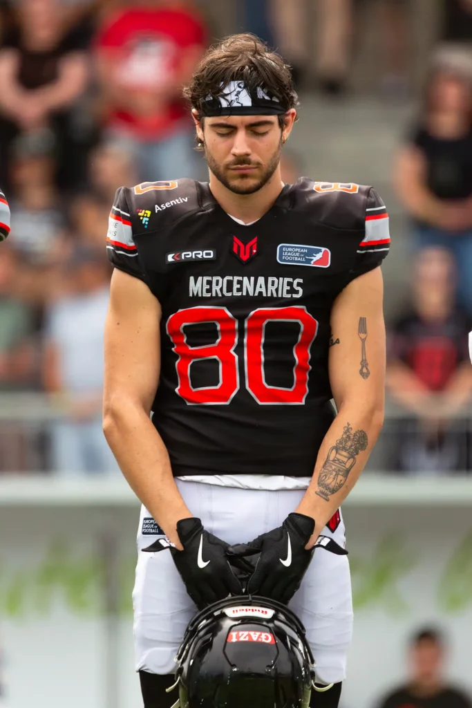 Football player in uniform with head down, holding helmet.