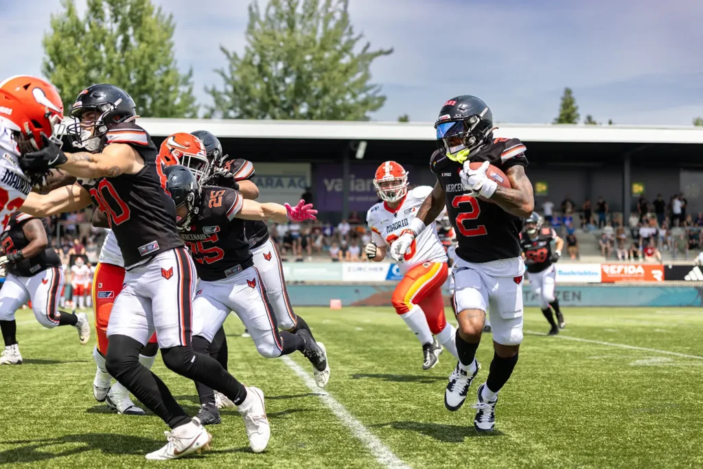 Football player #2 of the Mercenaries runs with ball, defenders close in.