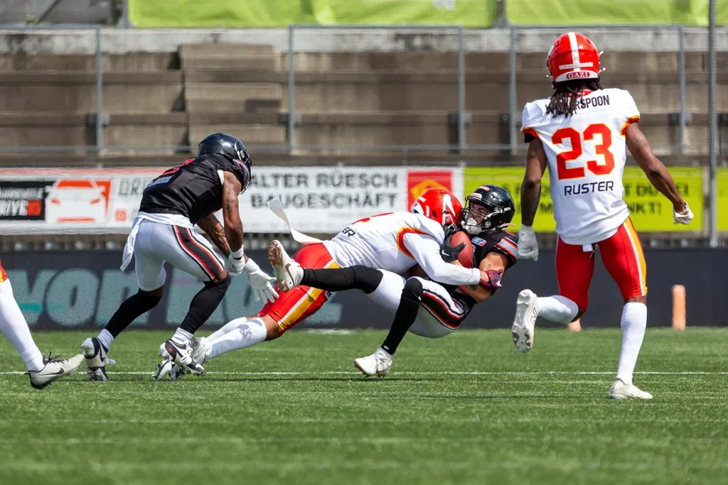 Football player tackled hard during a fast-paced game on green turf.