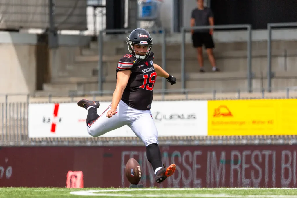 Football kicker in mid-kick wearing a black and red uniform.