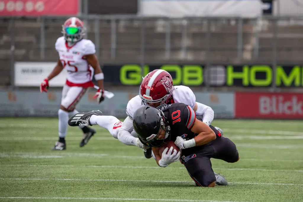 Football player tackled mid-play during a football game on green turf.