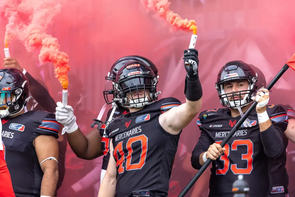 Football players in black uniforms celebrate with red smoke and team flag.