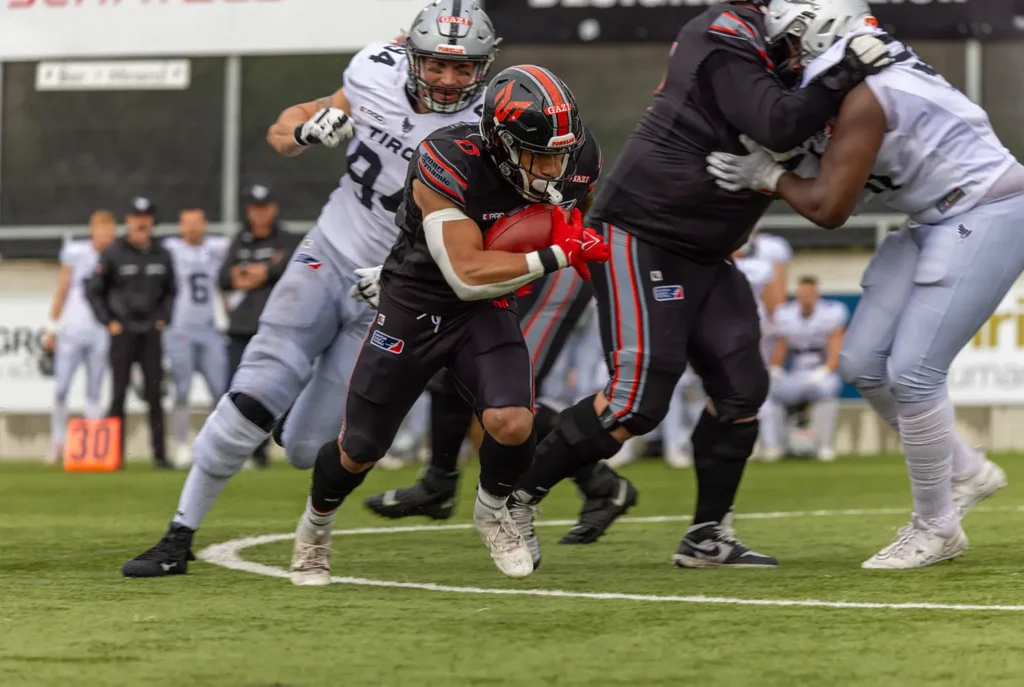 Football player running with the ball, pursued by defenders.