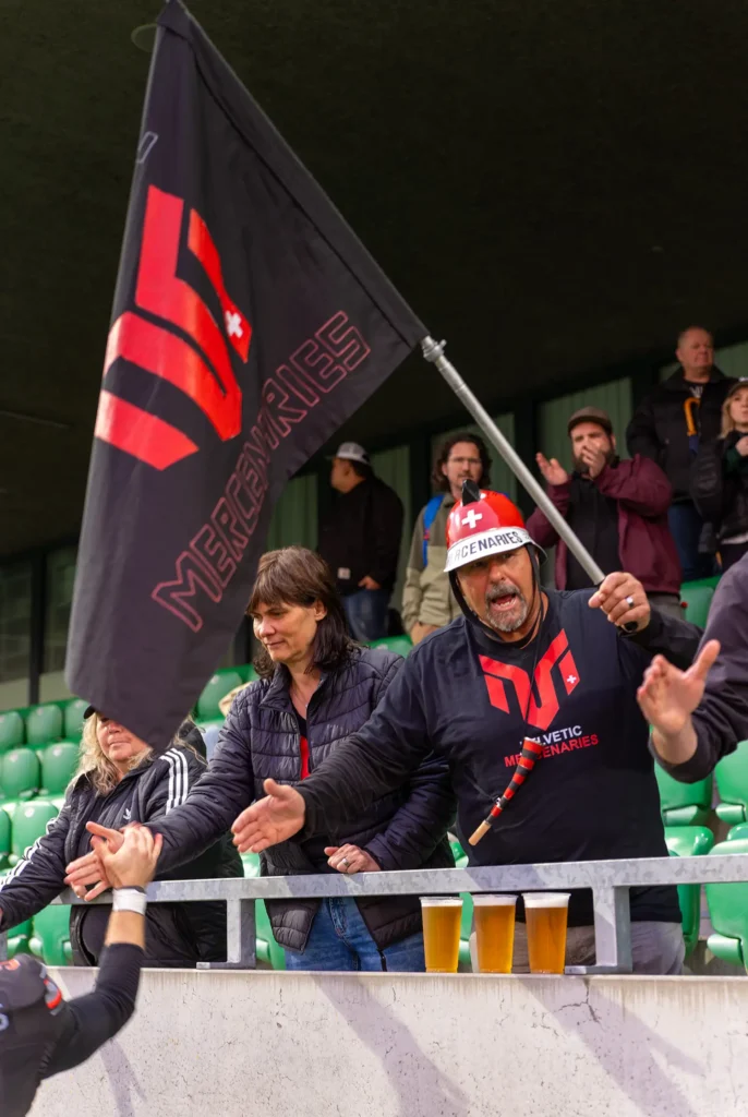 Fan with helmet waves flag, cheers Helvetic Mercenaries