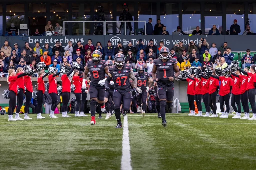 Football team runs onto field as cheerleaders wave pom-poms.