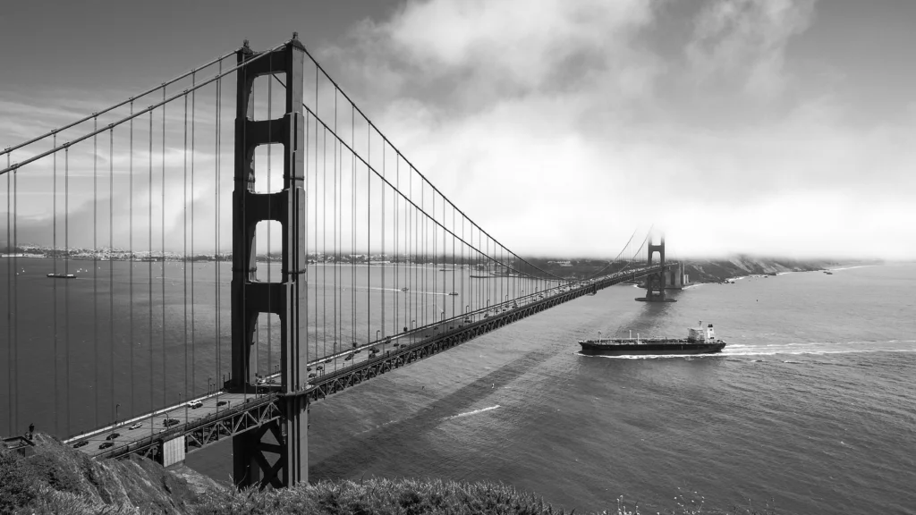 Black and white image of Golden Gate Bridge with passing cargo ship