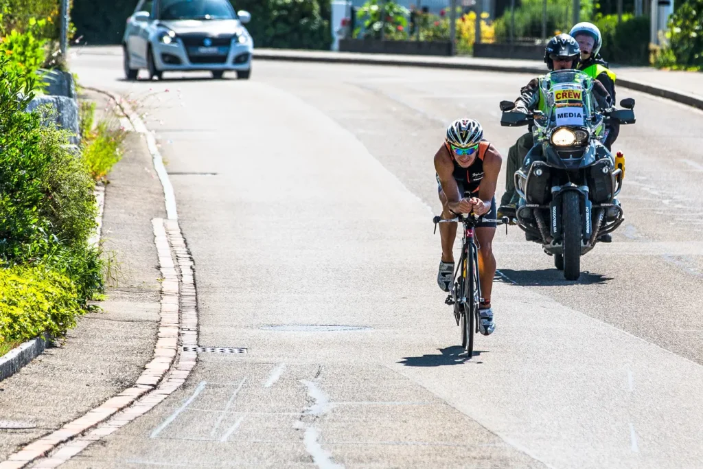 Triathlon cyclist in aero position on road accompanied by a media crew motorcycle