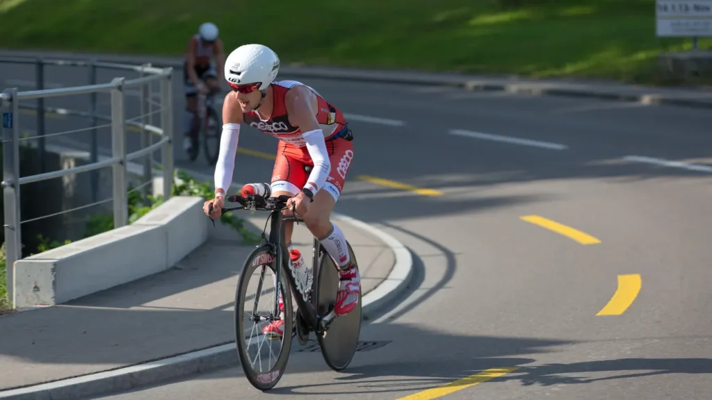 Triathlon cyclist in red Coop kit riding a time trial bike in aerodynamic position on a Swiss road