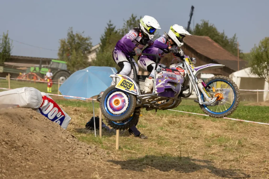 Purple sidecar motocross team number 859 catching air over a jump on a dirt track