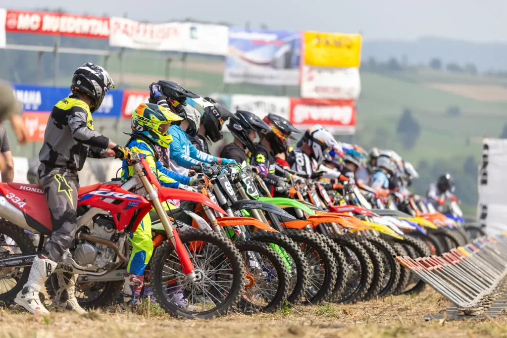 Row of motocross riders lined up at the starting gate with their dirt bikes ready to race