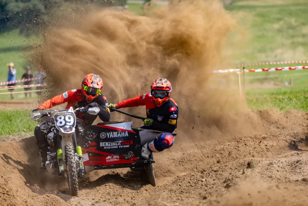 Two motocross riders battling for position on a dirt track, kicking up a cloud of dust, rider number 89 on a Yamaha in the foreground