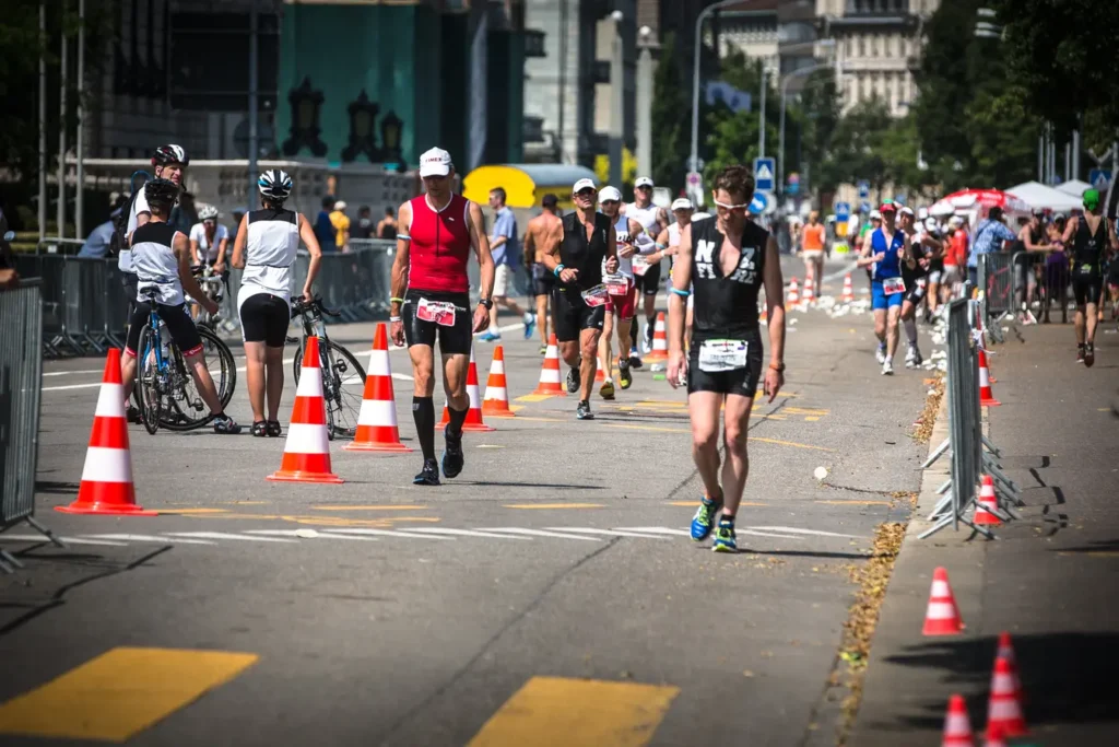 Triathletes running and walking through a city transition zone marked with orange traffic cones