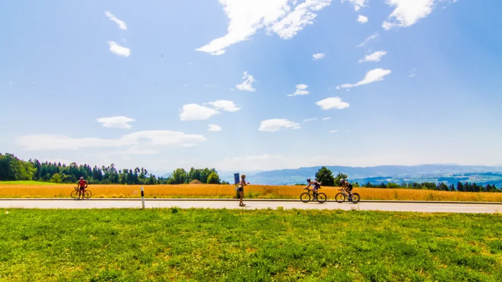 Cyclists riding along a country road with golden wheat fields and mountains in the background during a triathlon