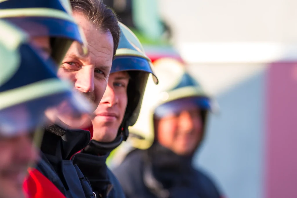 A row of focused firefighters in helmets and gear looking forward.