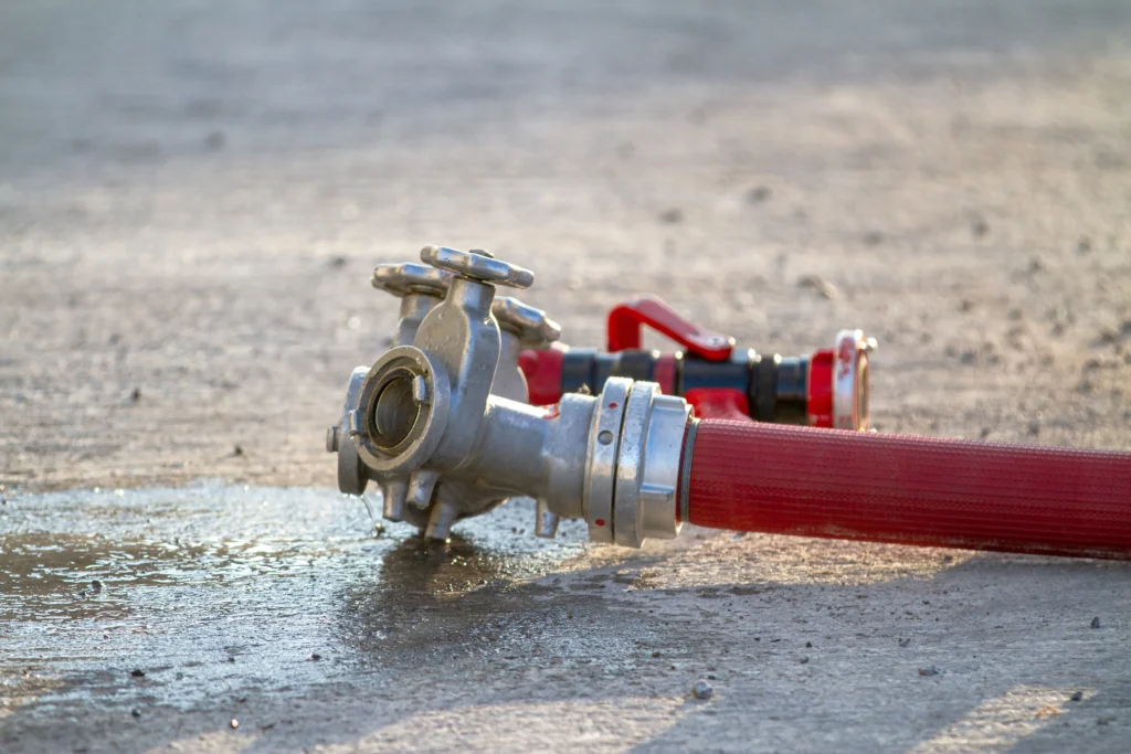 Close-up: fire hose manifold, nozzle laying on wet pavement, silver and red.