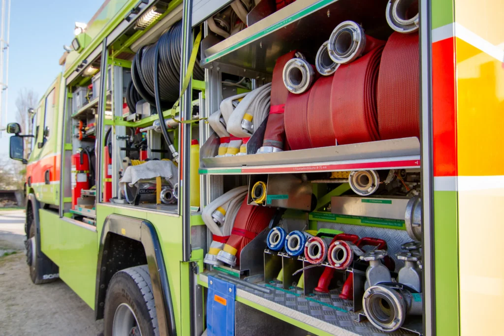 Open fire truck compartment showcasing red hoses, nozzles, and rescue tools.